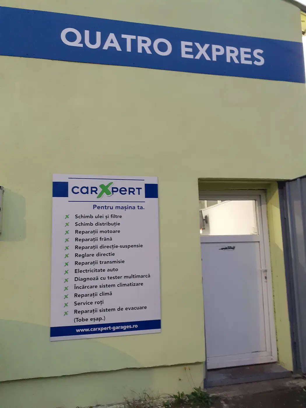 Fațada service-ului Quatro Expres, cu firma albastră și lista de servicii CarXpert pe perete