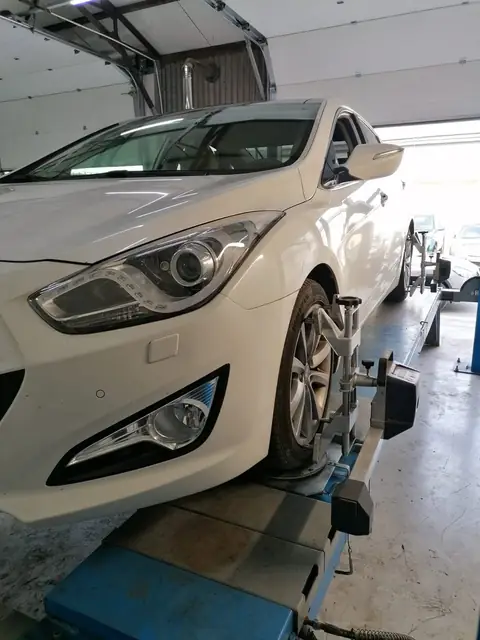Autoturism alb pe standul de geometrie, cu ținta 3D prinsă pe roata din față